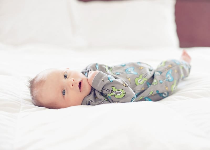 A baby in guitar-print pajamas resting on soft white bedding